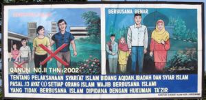Dress guidelines in Banda Aceh (Indonesia). The text at the bottom reads: Following the leading Islam principles according to article 13, paragraph 1, every Muslim has to wear Islamic clothing. Whosoever does not follow these accepted Islamic customs will be punished with Tazir crime.