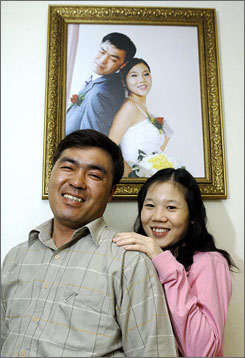 Kim Choong-Hwan, left, 40, a South Korean truck driver, poses with his Vietnamese wife Ngo Ngoc Quy Hong, 21, in front of their wedding photo in Osan, 34 miles south of Seoul. Kim is among a growing army of South Korean and Japanese bachelors or divorcees who have turned to less wealthy Asian countries for brides.