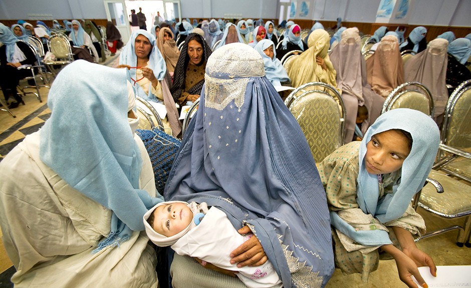 A woman wearing a burka and holding her baby joins hundreds of others to pray for peace to commemorate International Women's Day in Kandahar City, one of the most volatile parts of Afghanistan.  Despite the overwhelmingly female presence in the room, she wears a burka to protect her identity from the small number of men and members of the media in attendance.