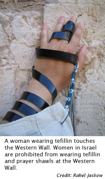 A woman wearing tefillin touches the Western Wall. Women in Israel are prohibited from wearing tefillin and prayer shawls at the Western Wall.