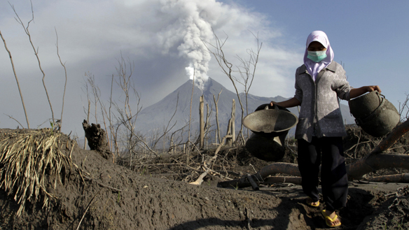 Mount Merapi volcano spews ash as a villager collects her valuables from the ruins of her house at Kali Tengah village in Sleman, near Yogyakarta, on Monday. 