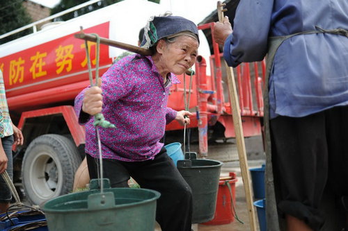 Luo Jinmei, 81, carries 10-kilogram buckets on her shoulders. Both her sons have left home to work and she lives alone. [sxdaily.com.cn]