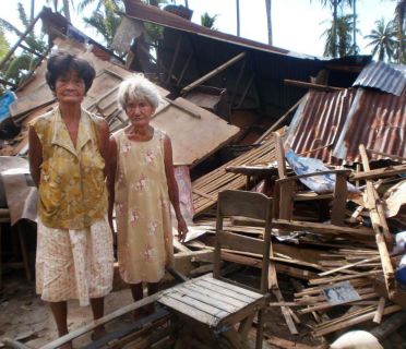 An older woman and her mother stand beside their home that was destroyed by Typhoon Haiyan.