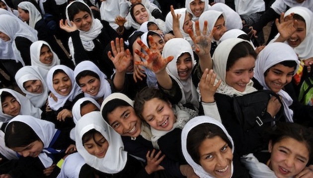 UNICEF Image: Smiling school girls raise their hands to the camera. 