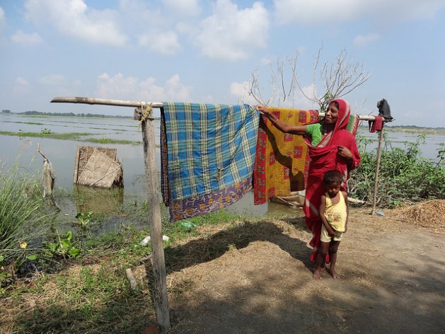 A woman dries blankets after her home went underwater for five days in one of the villages of India's Morigaon district. The woven bamboo sheet beyond the clothesline used to be the walls of her familys toilet. Credit: Priyanka Borpujari/IPS