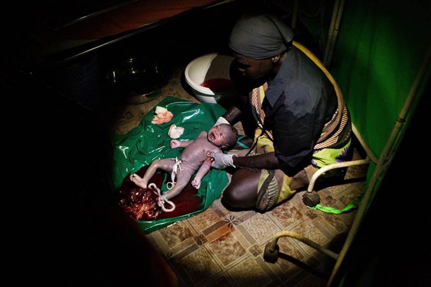 A midwife tends to a newborn baby girl born onto a tarpaulin on the floor, completely in the dark except for a torchlight