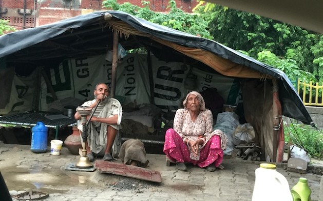 An elderly Indian couple sits outside their home, a barebones dwelling constructed from plastic sheeting and scrap material. Credit: Neeta Lal/IPS